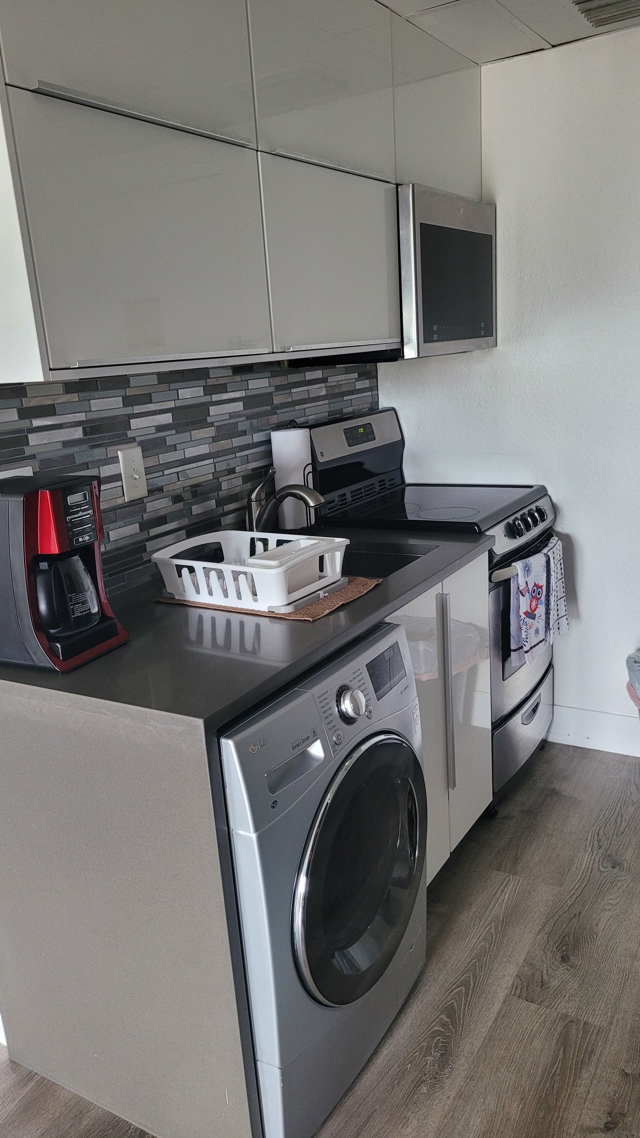 Une cuisine compacte équipée d’un lave-linge et d’un sèche-linge intégrés, d’une machine à café et d’un four à micro-ondes.