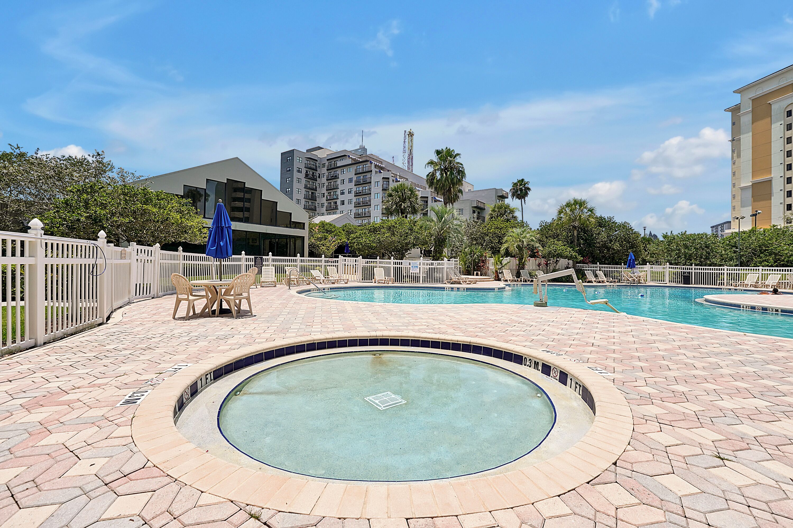 A swimming pool area with two pools, a white fence, and a building in the background.