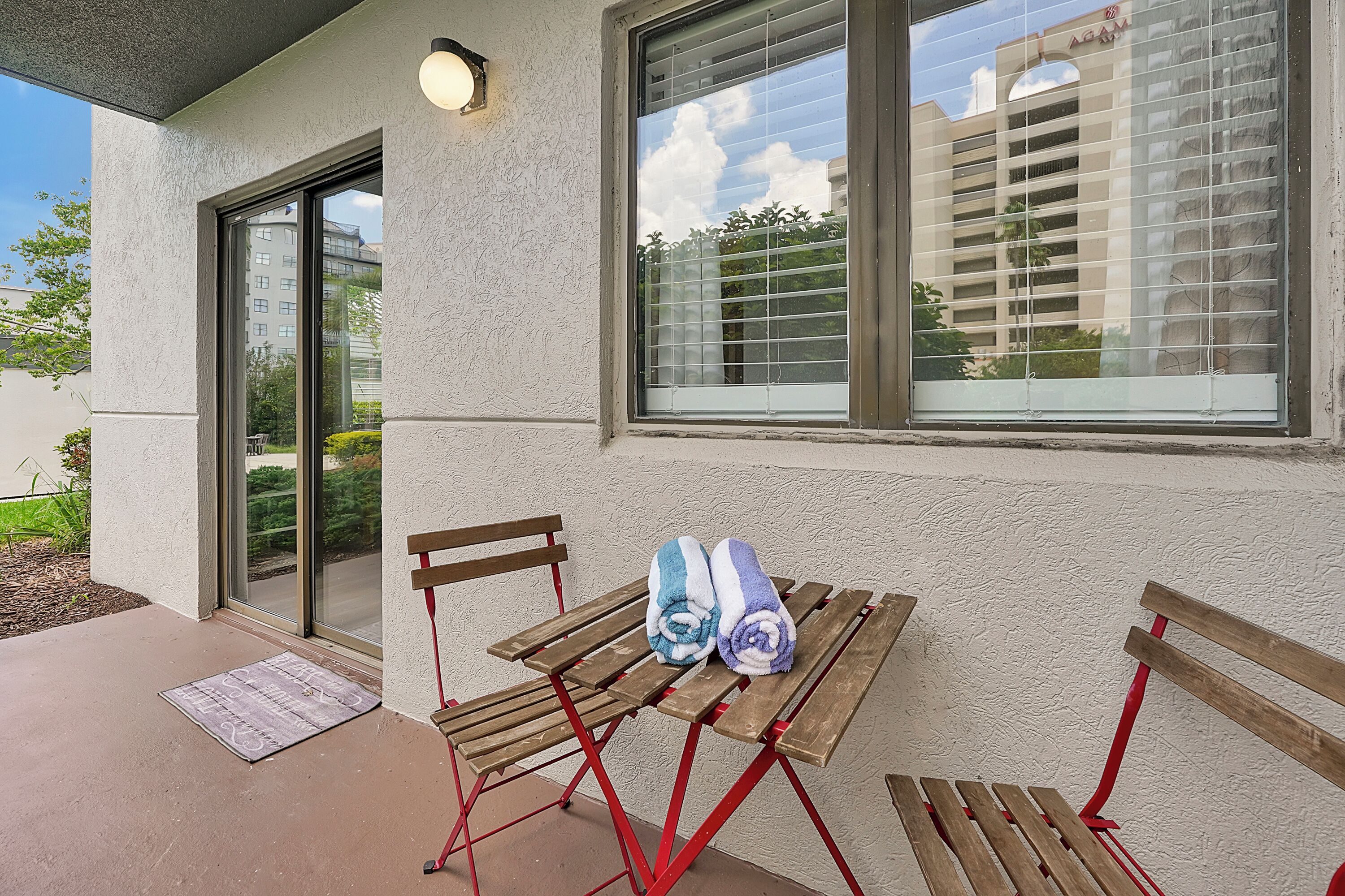 A patio with a wooden table and benches, a door, and a window with blinds.