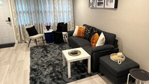 A modern living room with a sofa, a coffee table, and a chair. There is a door and a window with curtains. - Newly Renovated Luxury 2-BD 2-BA house, AC, WiFi. Mins to NYC, EWR, Newark Distr (Union)
