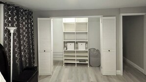 A walk-in closet with open doors, featuring multiple shelves and drawers, a hanging shoe rack, and a floor lamp. - Newly Renovated Luxury 2-BD 2-BA house, AC, WiFi. Mins to NYC, EWR, Newark Distr (Union)