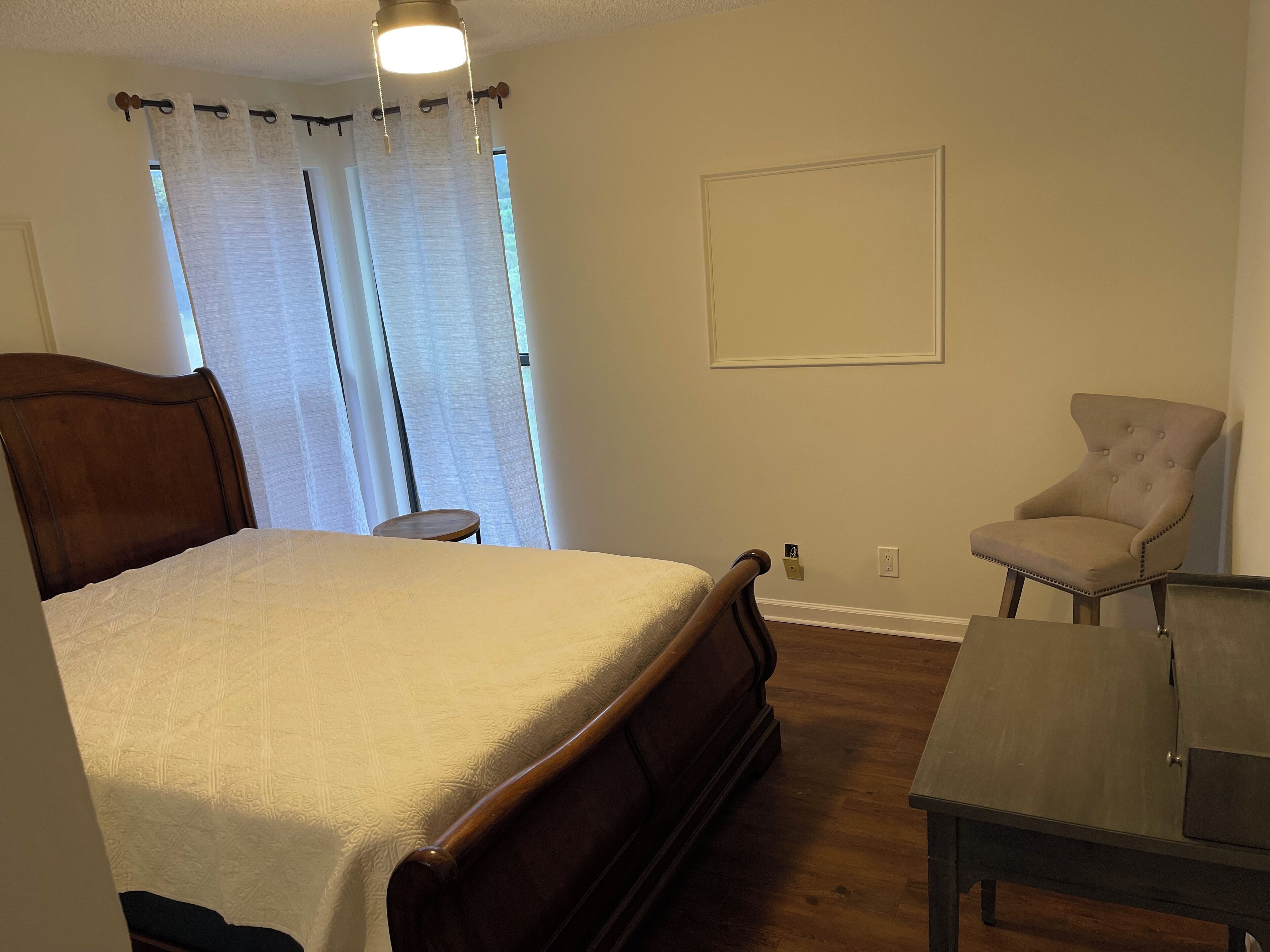 Een slaapkamer met een bed, een stoel, een klein tafeltje en een raam met gordijnen.