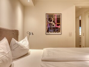 Habitación de hotel con cama, almohadas, una lámpara y un cuadro abstracto enmarcado en la pared.