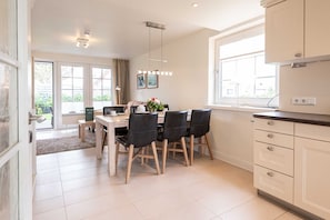 A modern kitchen with a dining area, featuring a large window, a built-in oven, and a light fixture above the table.