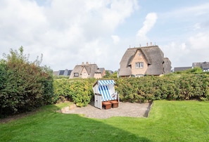 A traditional house with a thatched roof, surrounded by well-maintained hedges and a grassy lawn.