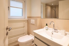 A modern bathroom with a toilet, a sink with a mirror, and a window above the toilet. - Strandhaus Whg. 1 - Strandnahe 3-zimmer Ferienwohnung auf ca. 55m² Wohnfläche, für bis zu 4 Personen (Wenningstedt-Braderup (Sylt))