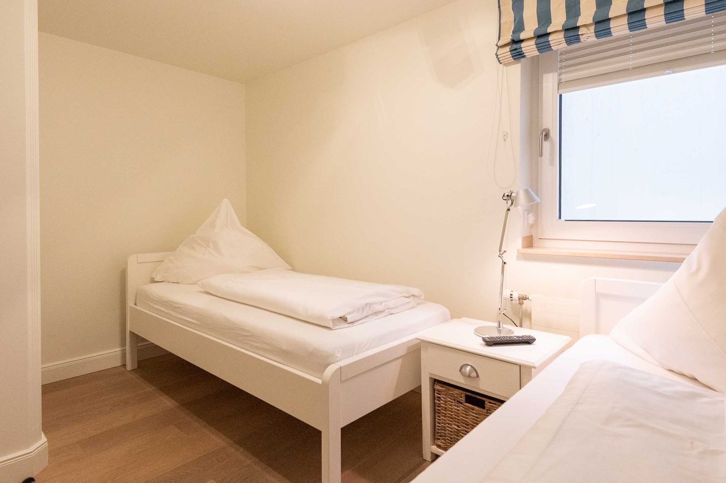 Un dormitorio pequeño y ordenado con una cama individual, una mesita de noche con lámpara y una ventana con persiana a rayas.