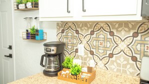 A kitchen with a coffee maker, a fruit basket, and decorative plants on shelves.