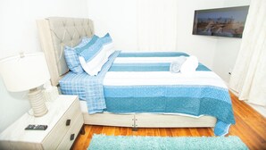 A neatly made bed with a blue and white checkered bedspread, a tufted headboard, and a bedside table with a lamp and remote control.
