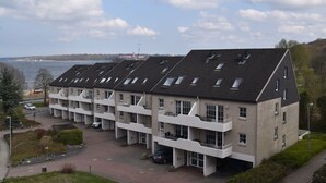 Ein mehrstöckiges Gebäude mit flachem Dach, großen Fenstern und Blick aufs Wasser.