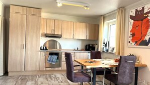 Eine kleine Küche mit Holzschränken, einem eingebauten Backofen und einem Essbereich mit Tisch und Stühlen.