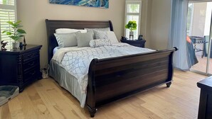 Une chambre avec un lit en bois foncé, un tableau abstrait bleu, une petite plante en pot et une table de chevet sur laquelle se trouvent un téléphone et un chargeur.