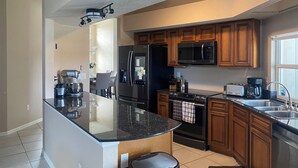 Une cuisine moderne dotée d’un îlot central, d’appareils électroménagers en acier inoxydable, de meubles de rangement en bois et d’un ventilateur de plafond.