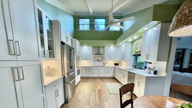 Una cocina moderna con armarios blancos, una mesa de comedor de madera y un ventilador de techo.