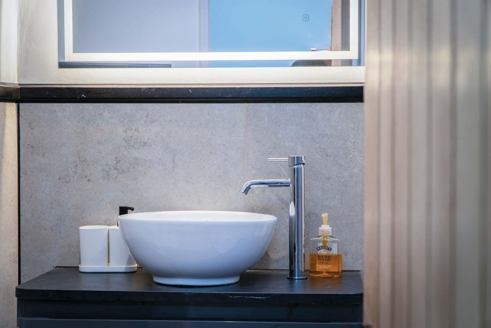 Une salle de bain avec un lavabo sur colonne blanc, un robinet chromé, un distributeur de savon et un petit flacon de savon pour les mains.