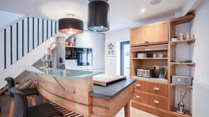 A modern kitchen with a glass island, wooden cabinetry, and a built-in stove. - The Cottage - 2 Bedroom Cottage - Tenby (Tenby)