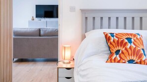 A bedroom with a bed, a nightstand with a lamp, a sofa, and a television in the background.