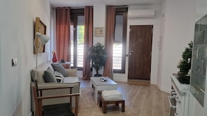 Una sala de estar con un sofá, una mesa de centro, una mesita, una planta y una puerta.
