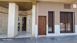 Entrada de un edificio con puerta de vidrio, puerta de madera y ventana con contraventanas.