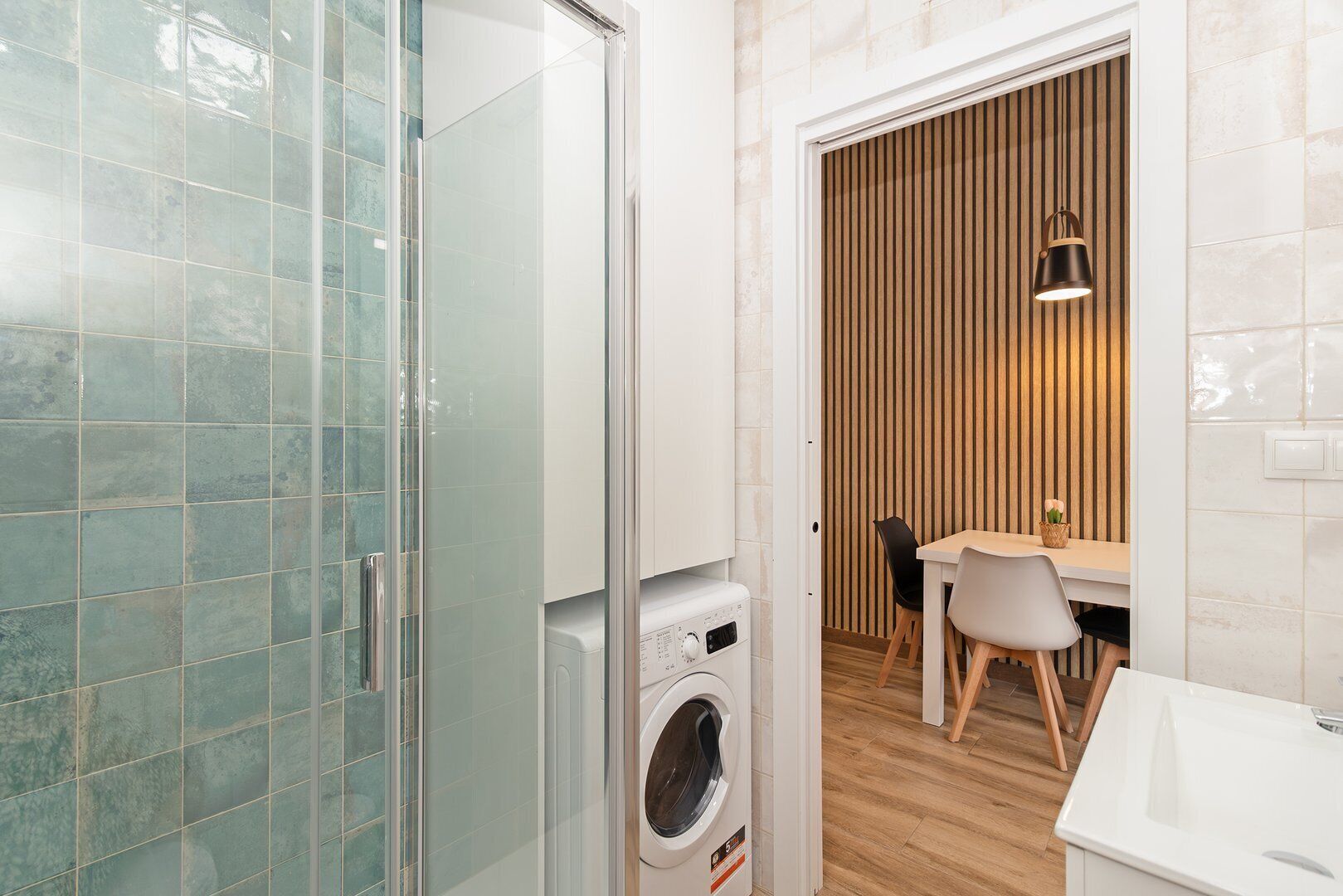 A modern bathroom with a glass shower enclosure, a washing machine, and a dining area with a wooden slat wall and pendant lighting.