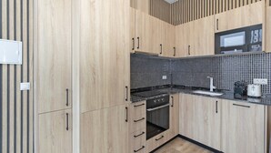 Een moderne keuken met houten kastjes, een zwart betegelde spatwand, een inbouwoven en een magnetron.