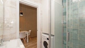 Ein kleines Badezimmer mit Waschbecken, Waschmaschine und Duschkabine aus Glas.