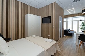 Ein modernes Hotelzimmer mit Bett, Fernseher, Kleiderschrank und einer Sitzecke mit Sofa und Tisch.