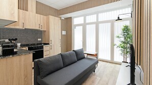 Una cucina moderna con mobili in legno, un piano di lavoro nero e un piano cottura integrato. Si nota un divano grigio e un tavolino con una pianta.