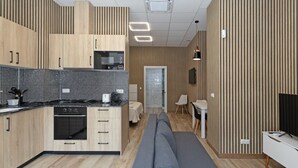 A modern kitchen with wooden cabinets, a black tiled backsplash, and a built-in oven. There is a grey sofa and a small dining area with a white table and chairs. - GuestReady Essential- Blissful stay near the beach (Valencia)