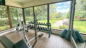 Een sportschool met fitnessapparatuur, grote ramen en uitzicht op een tuin.