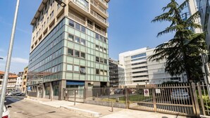 Un edificio moderno con facciata in vetro, un'area di parcheggio recintata e cielo sereno.