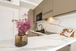A modern kitchen with a marble countertop, a built-in microwave, and a vase with purple flowers.