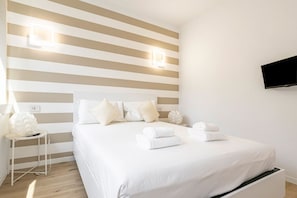 A hotel room with a striped wall, a bed with white linens, a bedside table with a lamp, and a mounted TV.