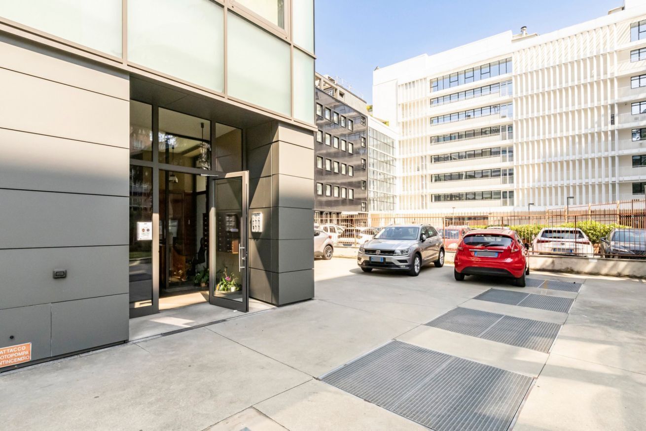 A modern building with a glass entrance, parked cars, and a clear sky.
