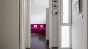 A hallway leading to a room with a pink sofa, white walls, and a window. - GuestHost - APT in the NOLO neighborhood! 500m from the M1 subway! (Milano)