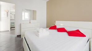 A modern hotel room with a large bed, white bedding, a white dresser, a mirror, and a beige accent wall. - GuestHost - APT in the NOLO neighborhood! 500m from the M1 subway! (Milano)