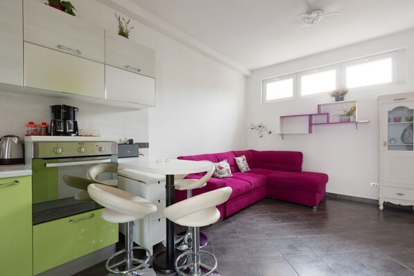 A compact kitchen with a dining area, a pink sofa, and a white cabinet.