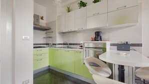 A modern kitchen with green cabinets, a white countertop, and a round dining table with two chairs. - GuestHost - APT in the NOLO neighborhood! 500m from the M1 subway! (Milano)