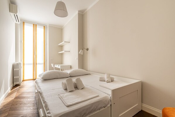 Un dormitorio con cama, mesitas de noche, un radiador y una ventana con cortinas.