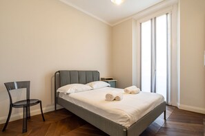 A bedroom with a bed, a chair, a nightstand, and a window with curtains.