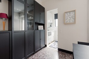Une cuisine avec des meubles de couleur sombre, une vitrine, une horloge et un carrelage à carreaux.