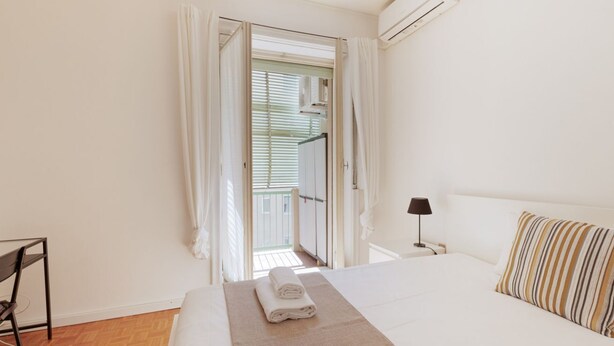 Un dormitorio con cama, mesita de noche, lámpara, ventana con cortinas y vistas al exterior.