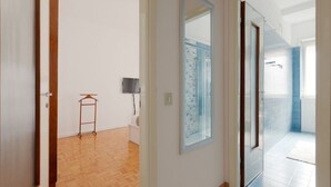 Un pasillo con suelo de madera, un espejo y una puerta que da a un baño con azulejos azules.