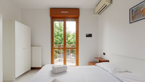 Ein Schlafzimmer mit Bett, Kleiderschrank, Heizkörper, Fenster mit Aussicht und einem Bild an der Wand.
