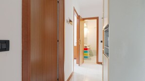 Ein Flur mit einer Holztür, einer weißen Wand und einem Blick auf ein Badezimmer mit Waschbecken und farbenfrohen Aufbewahrungsboxen.