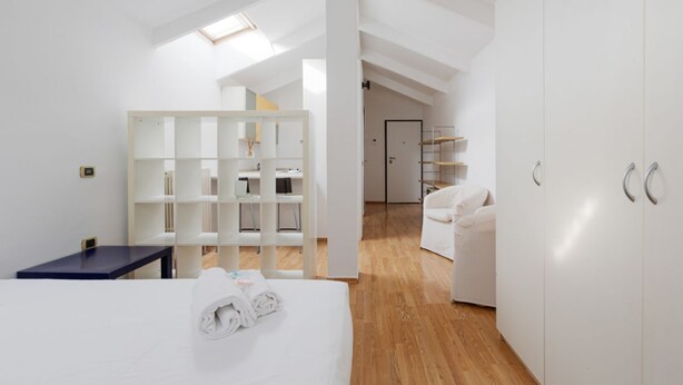 Ein modernes Hotelzimmer mit Bett, Schreibtisch, Kleiderschrank und einer weißen Regaleinheit.