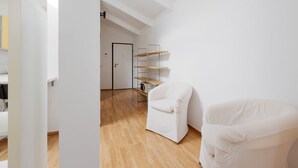Ein Zimmer mit einem weißen Stuhl, Holzboden, weißer Wand und einer Tür im Hintergrund.