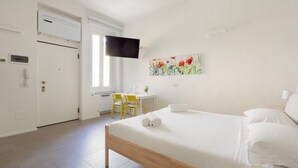 Ein Hotelzimmer mit einem Bett, einem Schreibtisch, einem Sessel, einem Fernseher und einem Bild an der Wand.