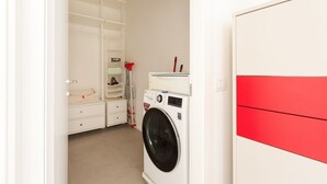Ein Waschbereich mit Waschmaschine, Wäscheständer und einem weißen Kleiderschrank mit roten Akzenten.
