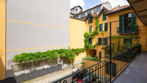 Ein Innenhof mit einem gelben Gebäude, grünen Fensterläden und einem schwarzen Geländer.